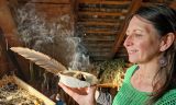KrÃ¤uterpÃ¤dagogin Jasmin Vigl verteilt den Rauch aus der RÃ¤ucherschale mit einer Feder.