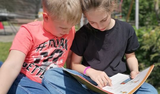 Ein Kind und ein Kind sitzen auf Gras und lesen ein Buch