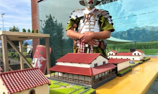 Eine Person in RÃ¼stung, die neben einem Modell von GebÃ¤uden steht