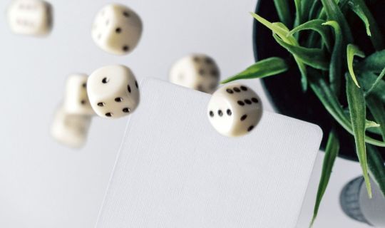 Würfel, die auf eine Karte fallen, mit einer Pflanze im Hintergrund Würfel, die auf eine Karte fallen, mit einer Pflanze im Hintergrund