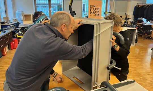 Drei Personen bauen gemeinsam einen FahrradanhÃ¤nger zusammen