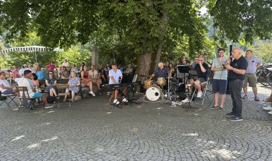Eine Gruppe von Menschen, die auf Bänken saÃen, und eine Person, die Instrumente spielte Eine Gruppe von Menschen, die auf Bänken saÃen, und eine Person, die Instrumente spielte