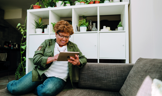ältere Frau sitzt am Sofa und macht etwas an ihrem Tablet ältere Frau sitzt am Sofa und macht etwas an ihrem Tablet