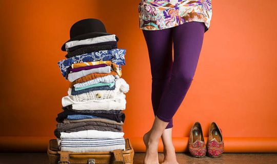 Das Foto zeigt einen Stapel Kleidungsstücke neben dem Unterkörper einer Frau. Das Foto zeigt einen Stapel Kleidungsstücke neben dem Unterkörper einer Frau.