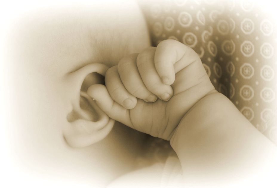 Eine Babyhand, die das Ohr eines Babys hÃ¤lt