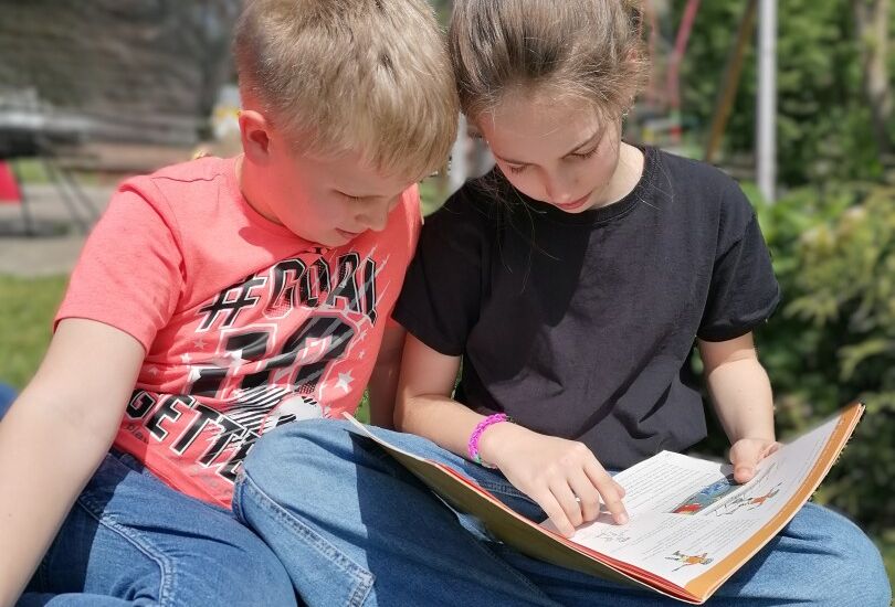 Ein Kind und ein Kind sitzen auf Gras und lesen ein Buch Ein Kind und ein Kind sitzen auf Gras und lesen ein Buch