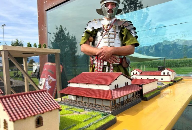 Eine Person in Rüstung, die neben einem Modell von Gebäuden steht Eine Person in Rüstung, die neben einem Modell von Gebäuden steht